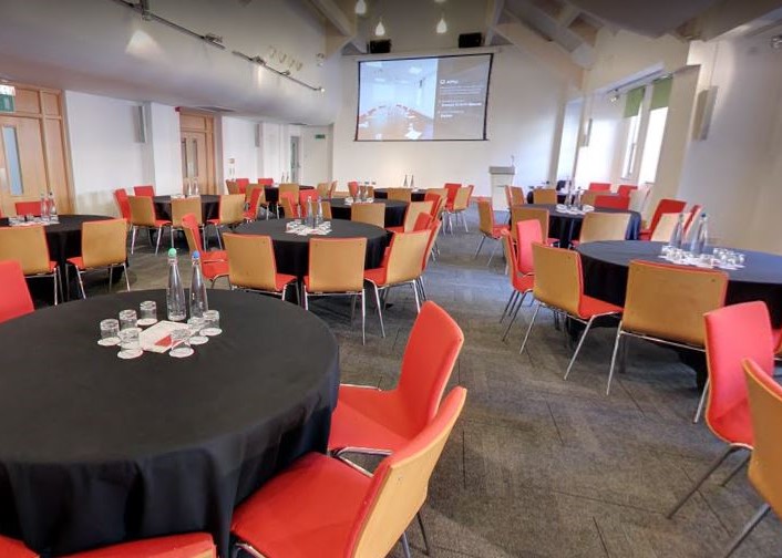 Explore, shown setup on round tables with chairs and screen for an event, which is where the main sessions will take place during the Women in Convenience event on 5 October 